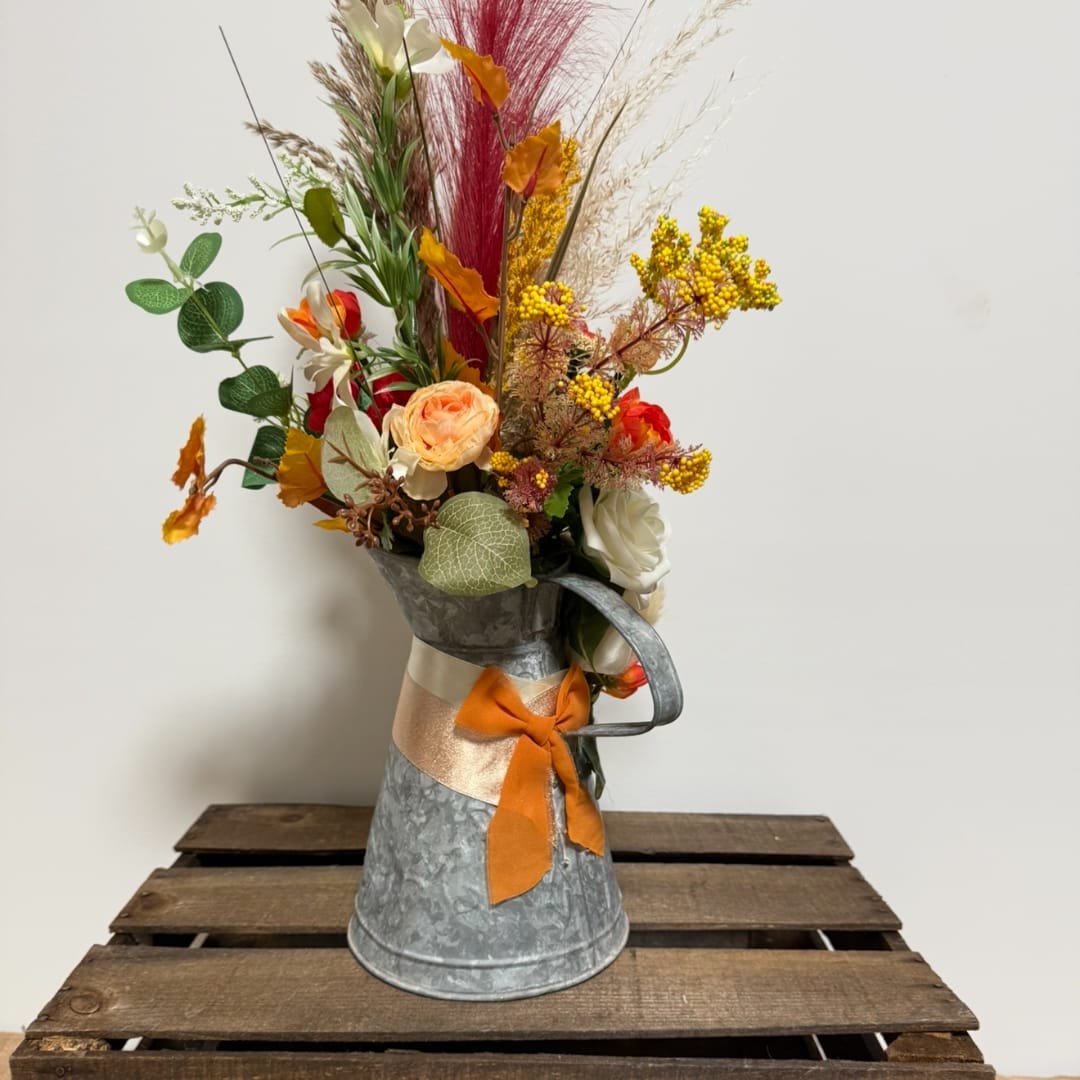 Tall floral arrangement in a metal pitcher with orange ribbon