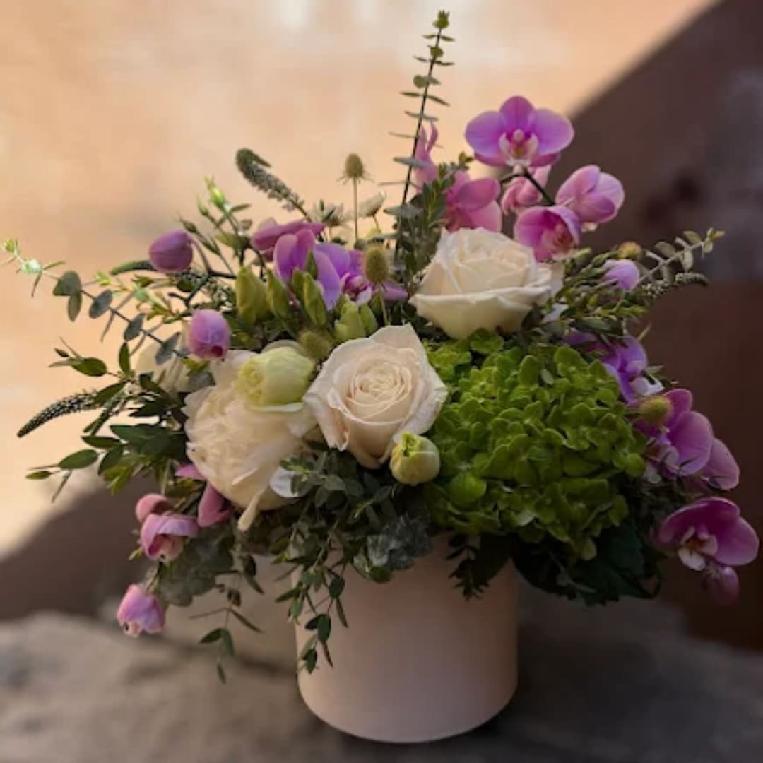 White roses and purple orchids in a white vase with greenery