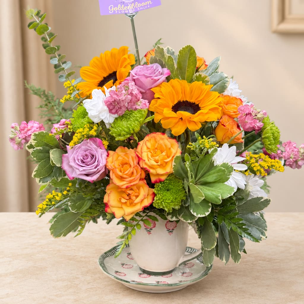 Mixed bouquet of sunflowers, roses, and daisies in a teacup vase