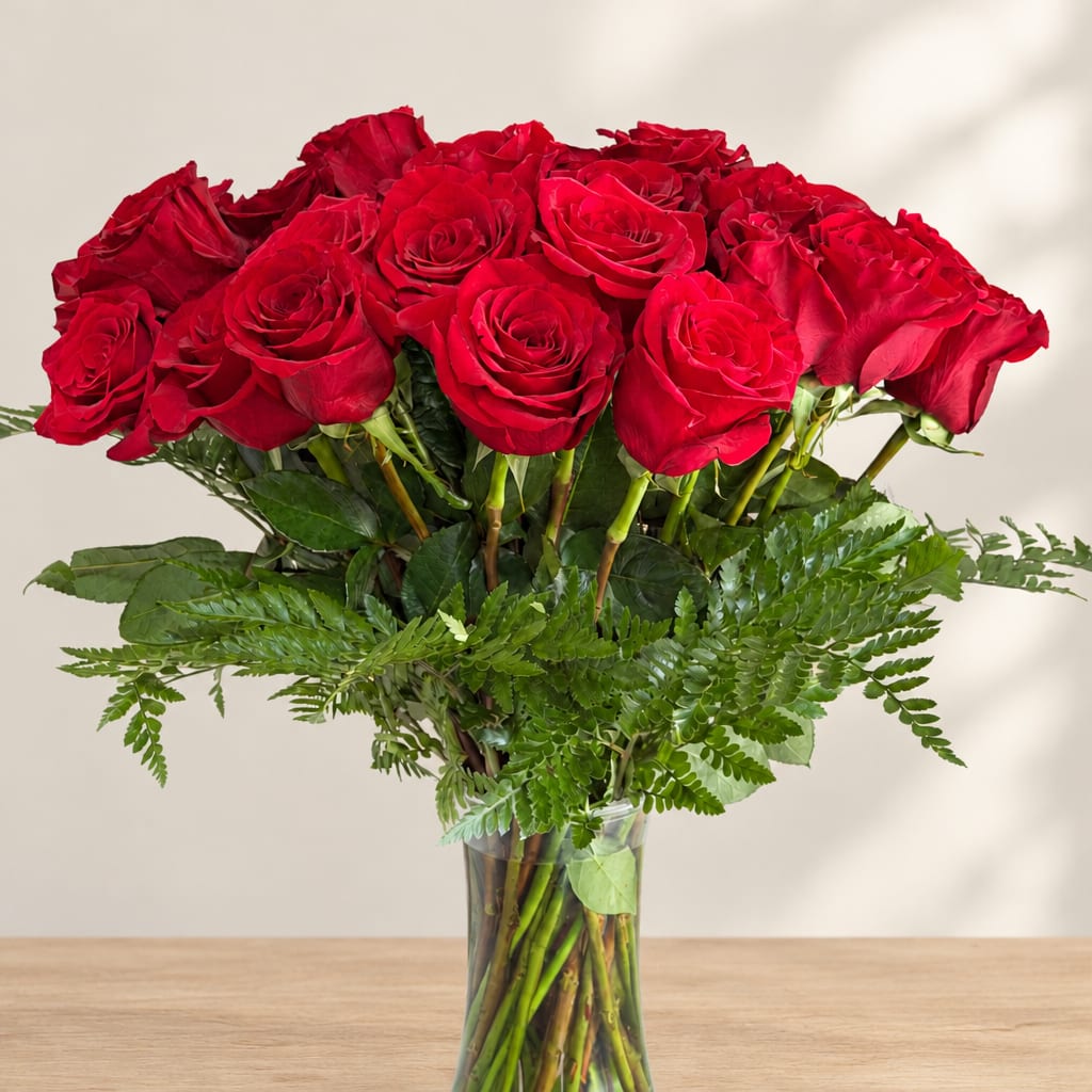 Red roses arranged in a clear glass vase with greenery