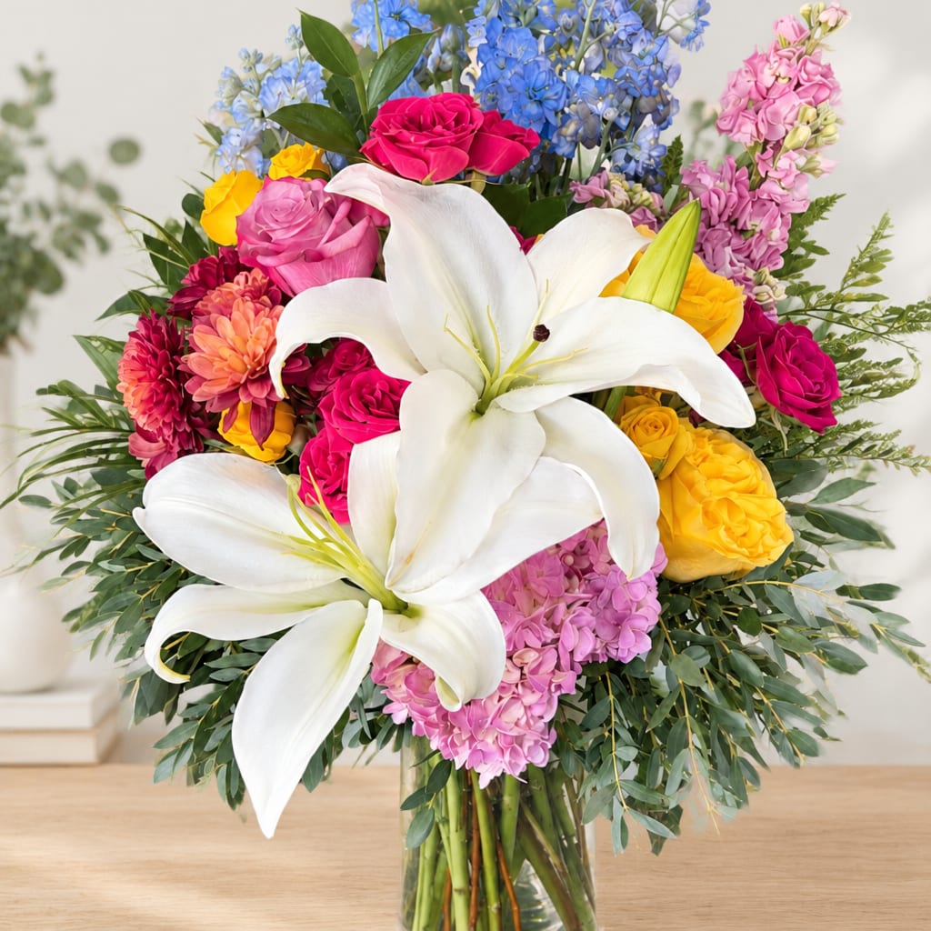 Colorful bouquet with white lilies, roses, and blue flowers in a glass vase