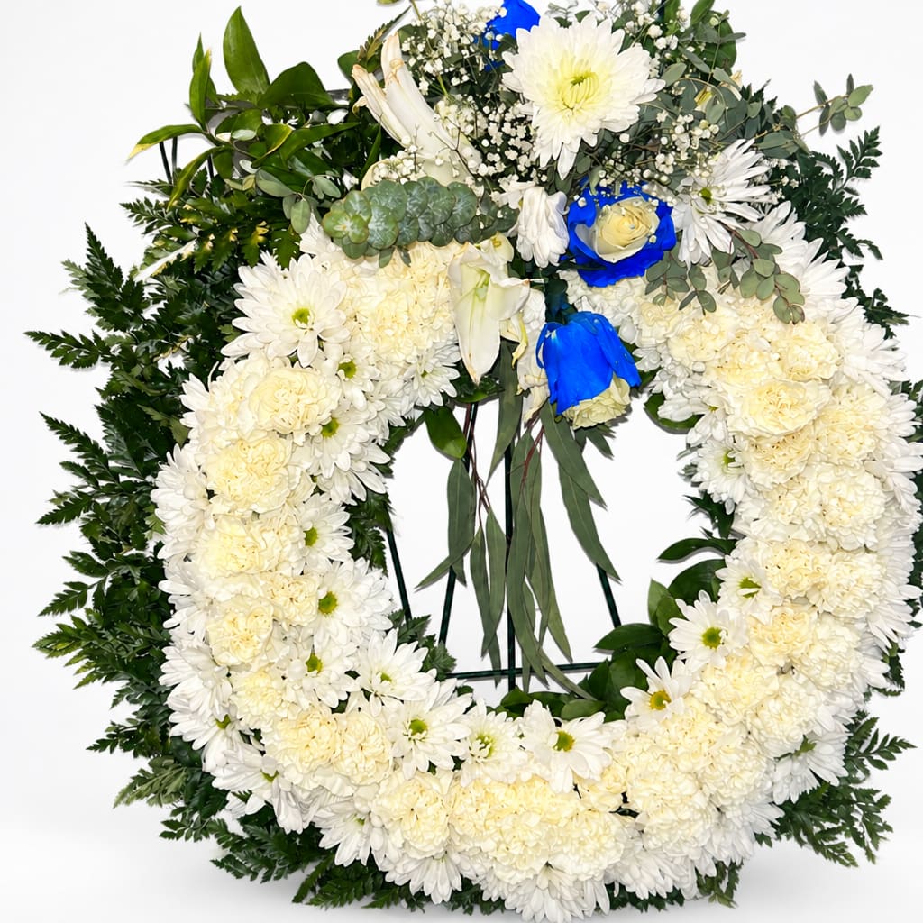 White floral funeral wreath with blue rose accents on a stand