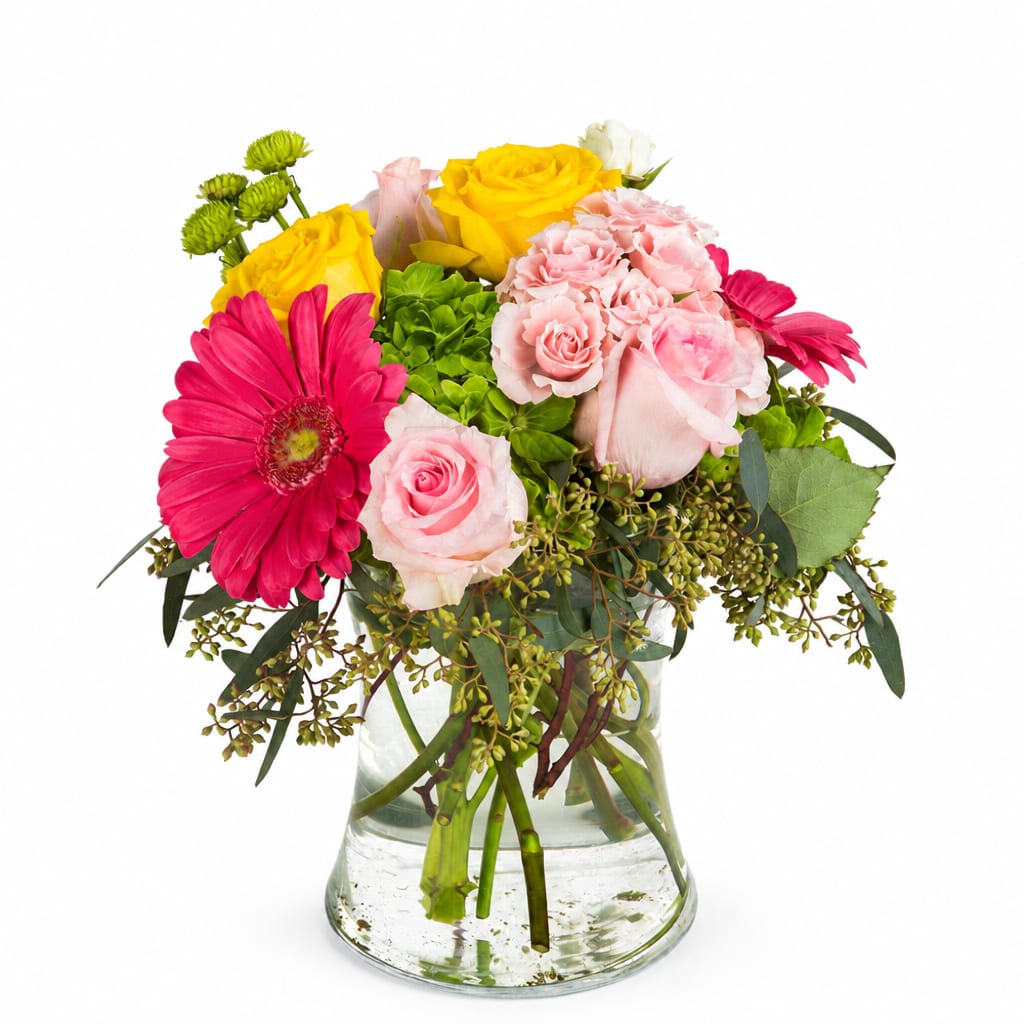 Mixed bouquet of pink, yellow, and white flowers in a clear glass vase