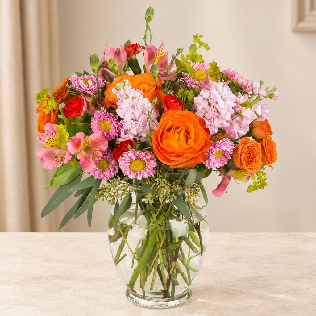 Mixed bouquet of orange, pink, and red flowers in a clear glass vase