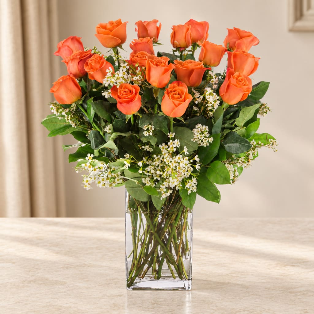 Orange roses arranged in a clear glass vase with small white filler flowers