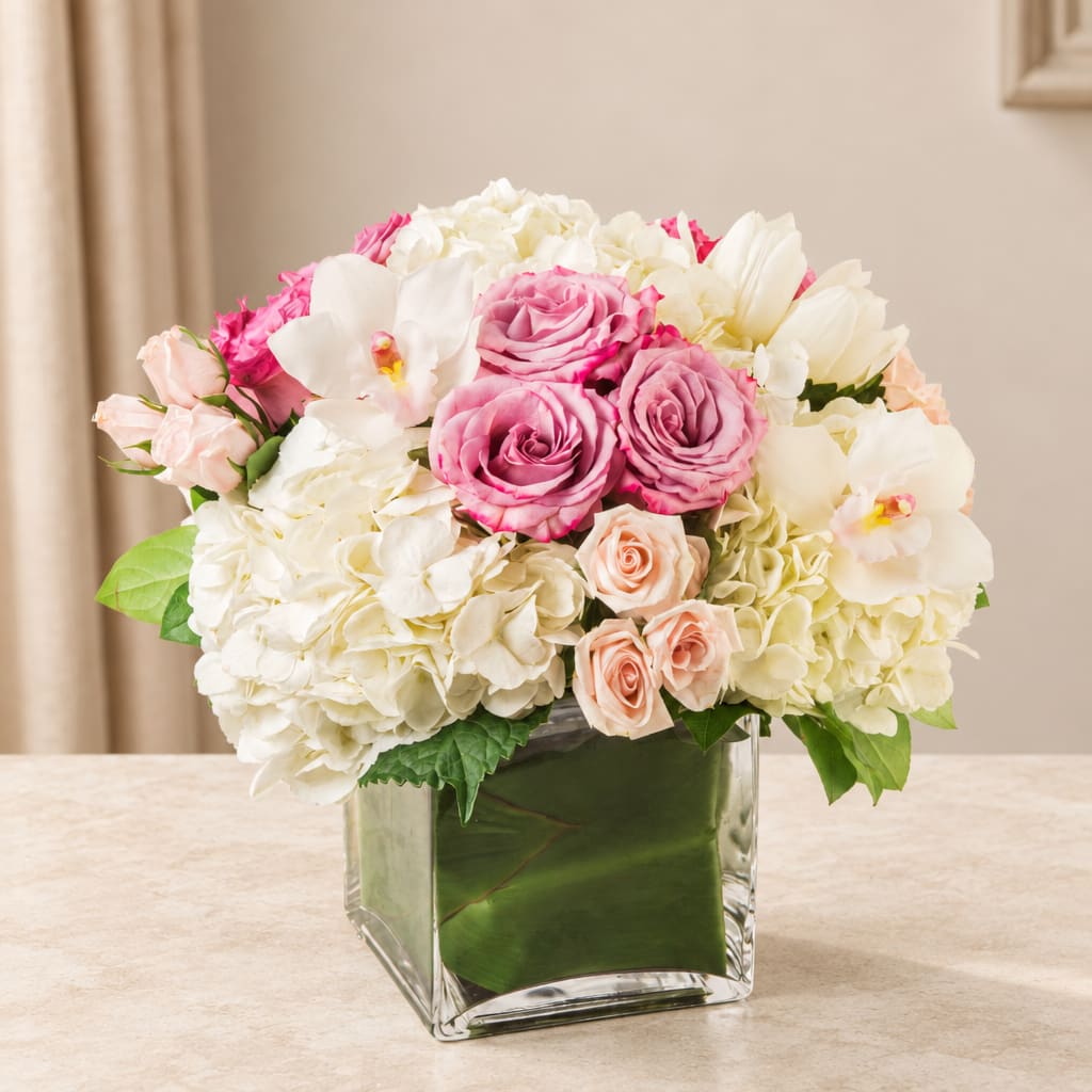 Pink and white roses with hydrangeas in a clear square vase