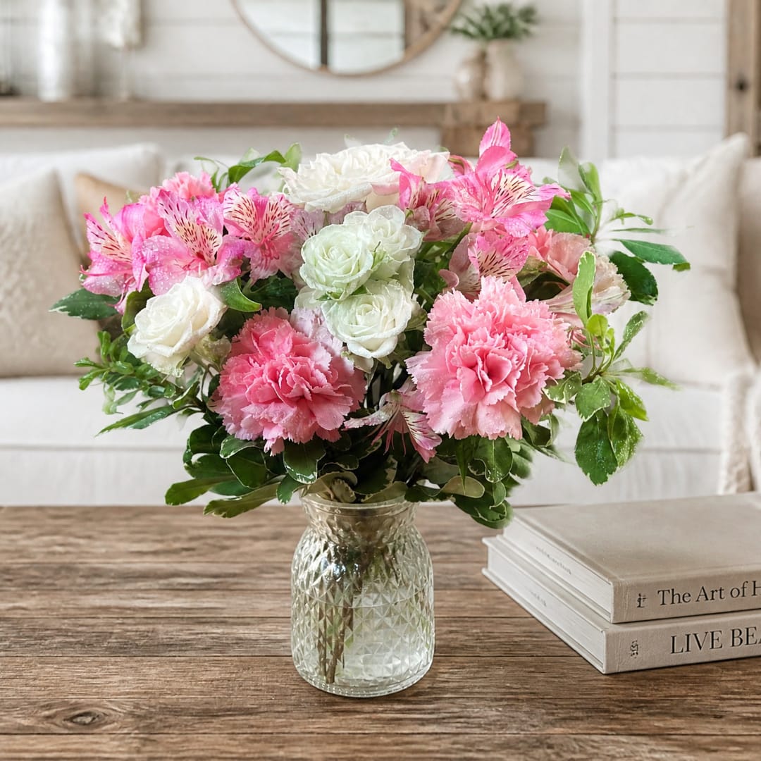 Pink and white flower arrangement in a clear glass vase on a table