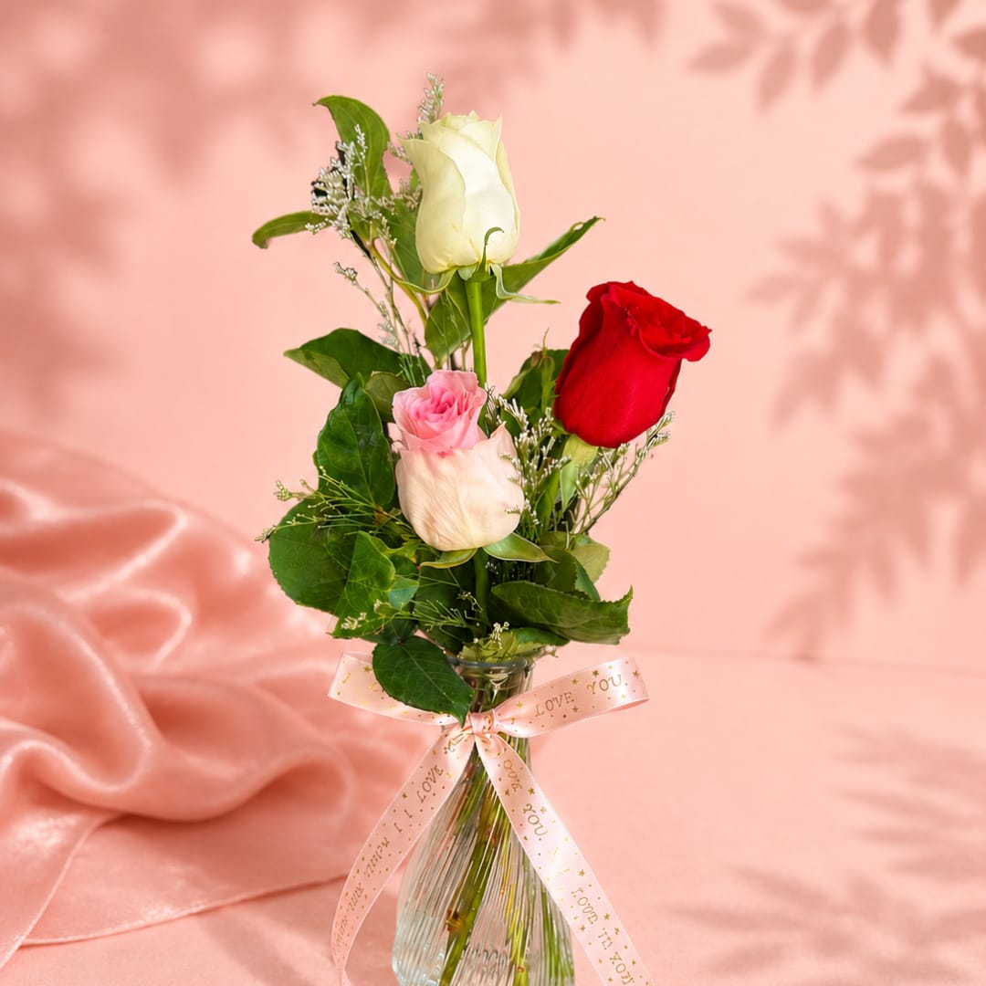 Three roses in a clear glass vase with a pink ribbon