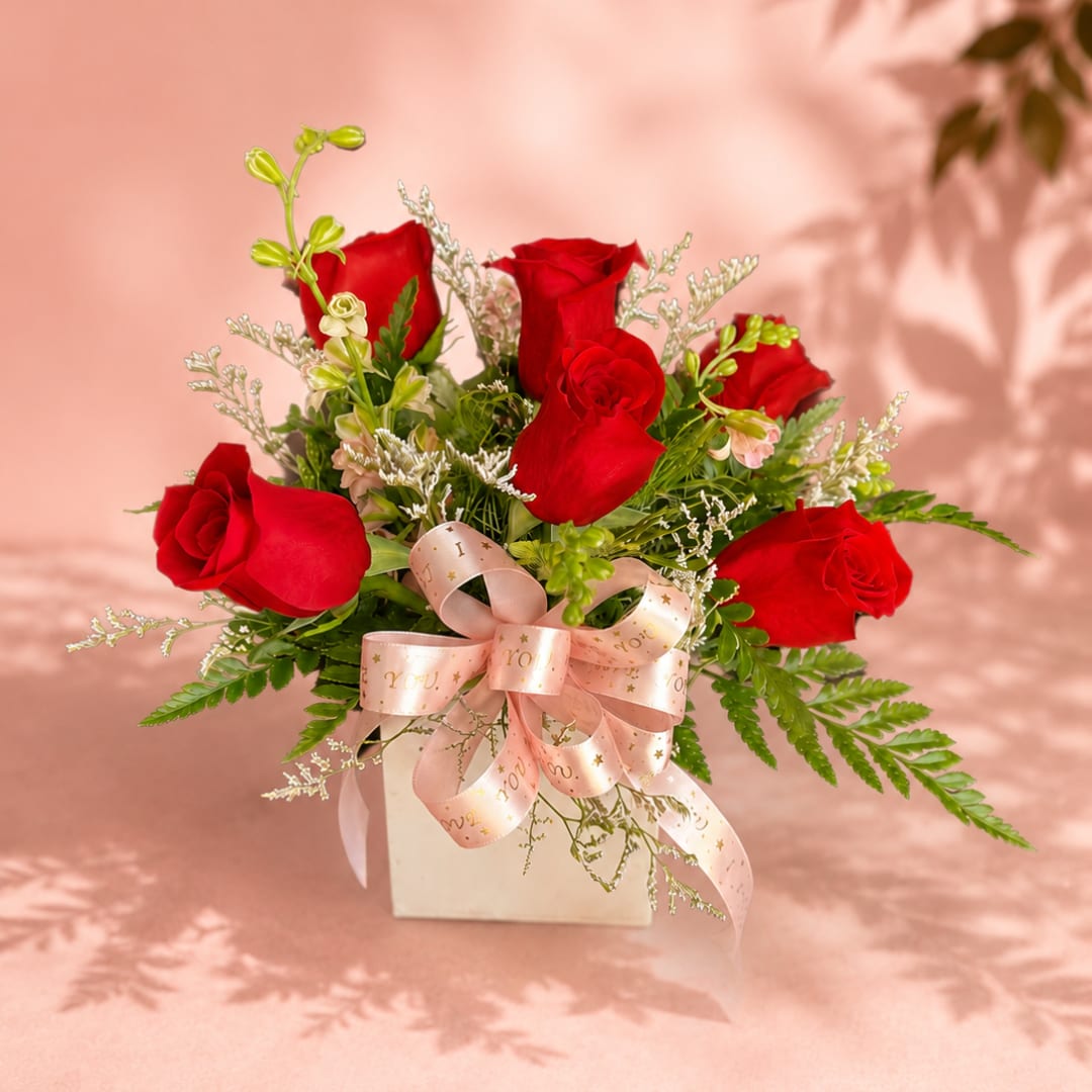 Red roses arranged in a white box with a pink ribbon bow