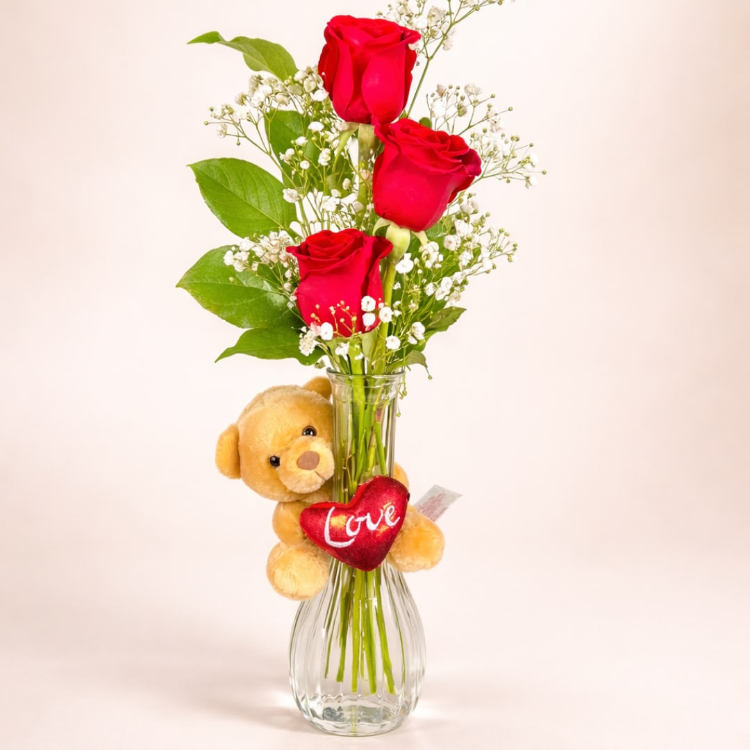 Red roses in a glass vase with a teddy bear and heart ornament