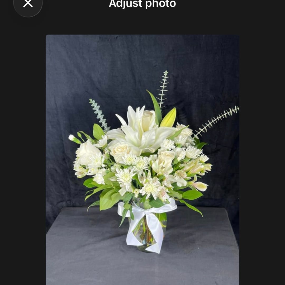White floral arrangement in a glass vase with a white ribbon