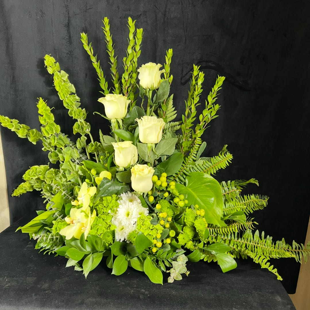 White roses and orchids arranged with bright green foliage against a black background