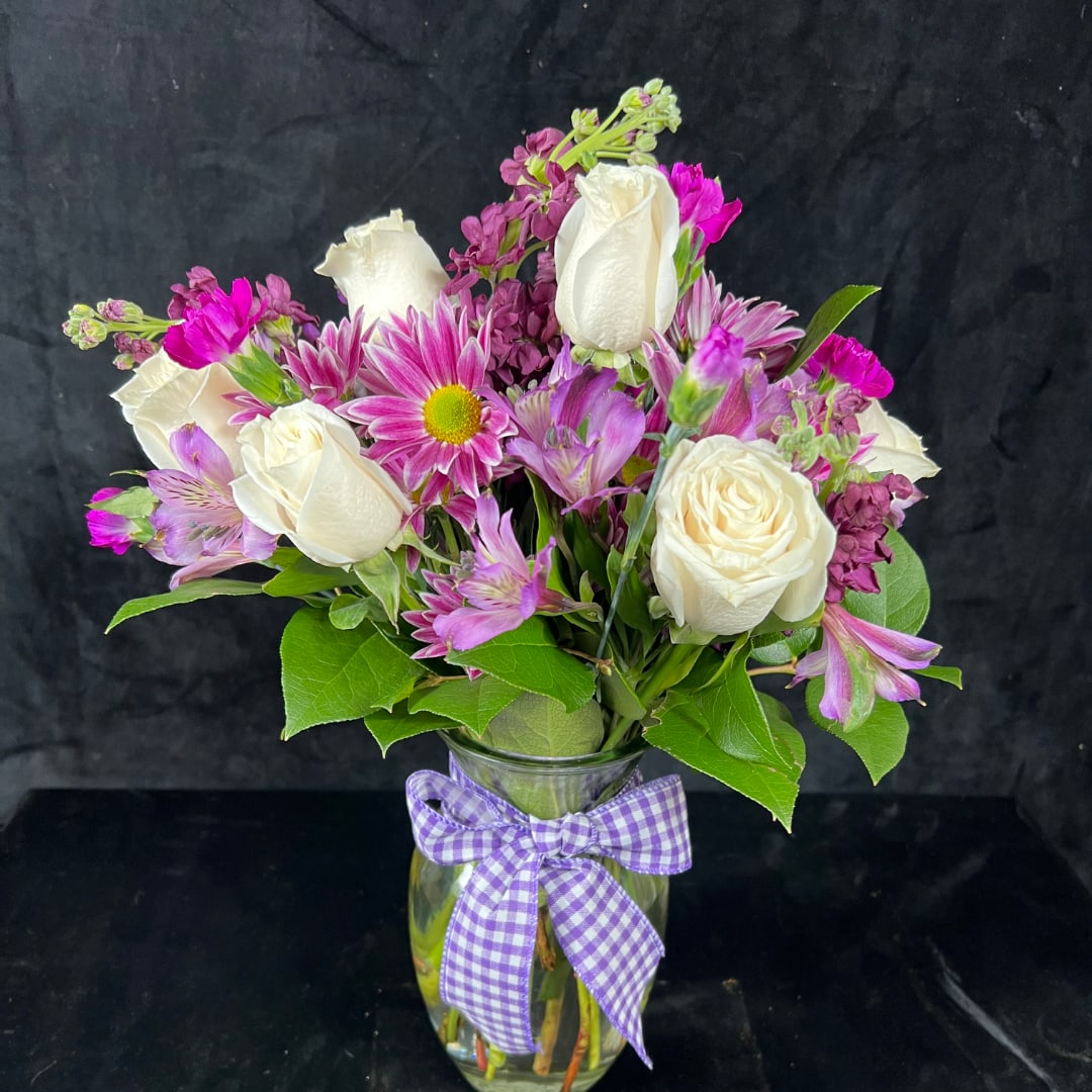 Pink and white mixed bouquet in a glass vase with a purple ribbon