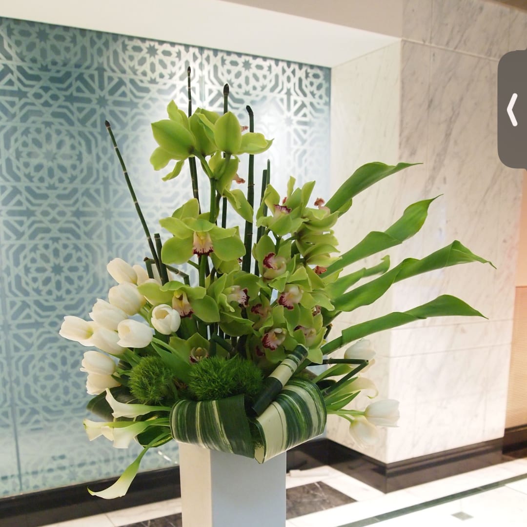 Green orchid arrangement with white tulips in a tall white vase