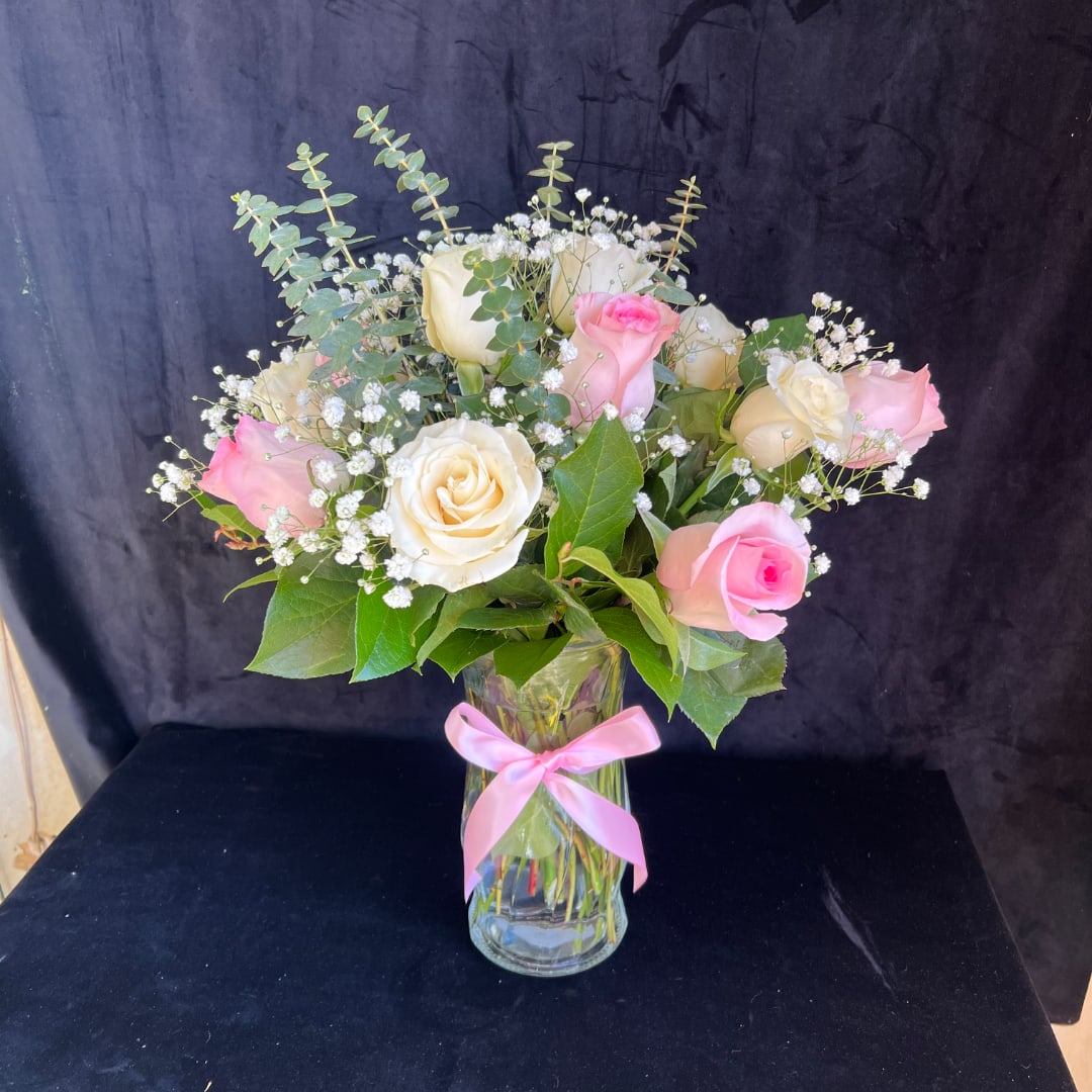 Pink and white roses in a glass vase with a pink ribbon