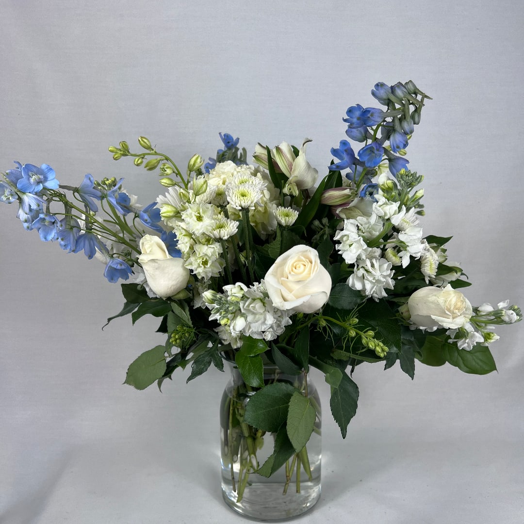 White roses and blue flowers arranged in a clear glass vase