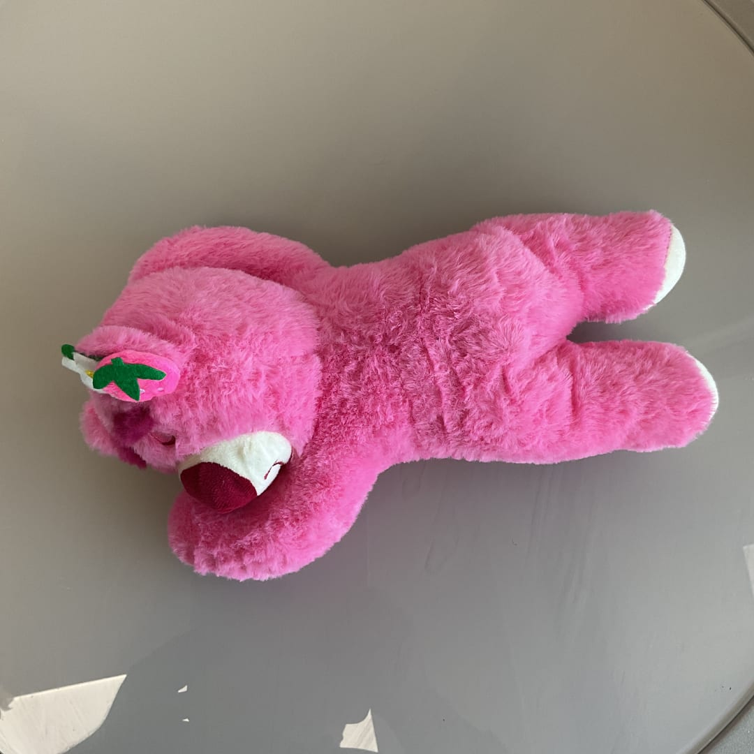 Pink plush teddy bear lying on a gray surface