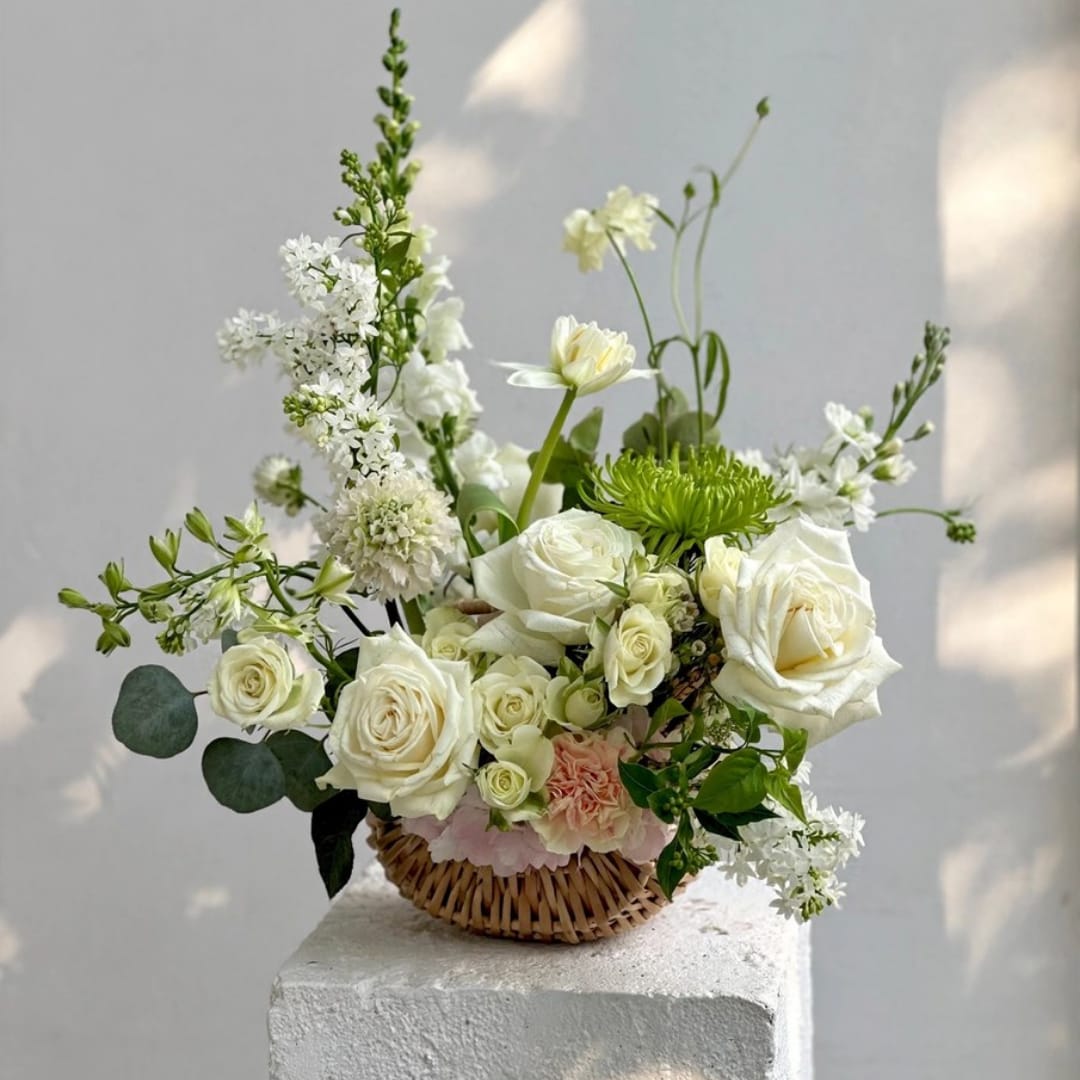 White rose bouquet in a woven basket with small white blooms and greenery