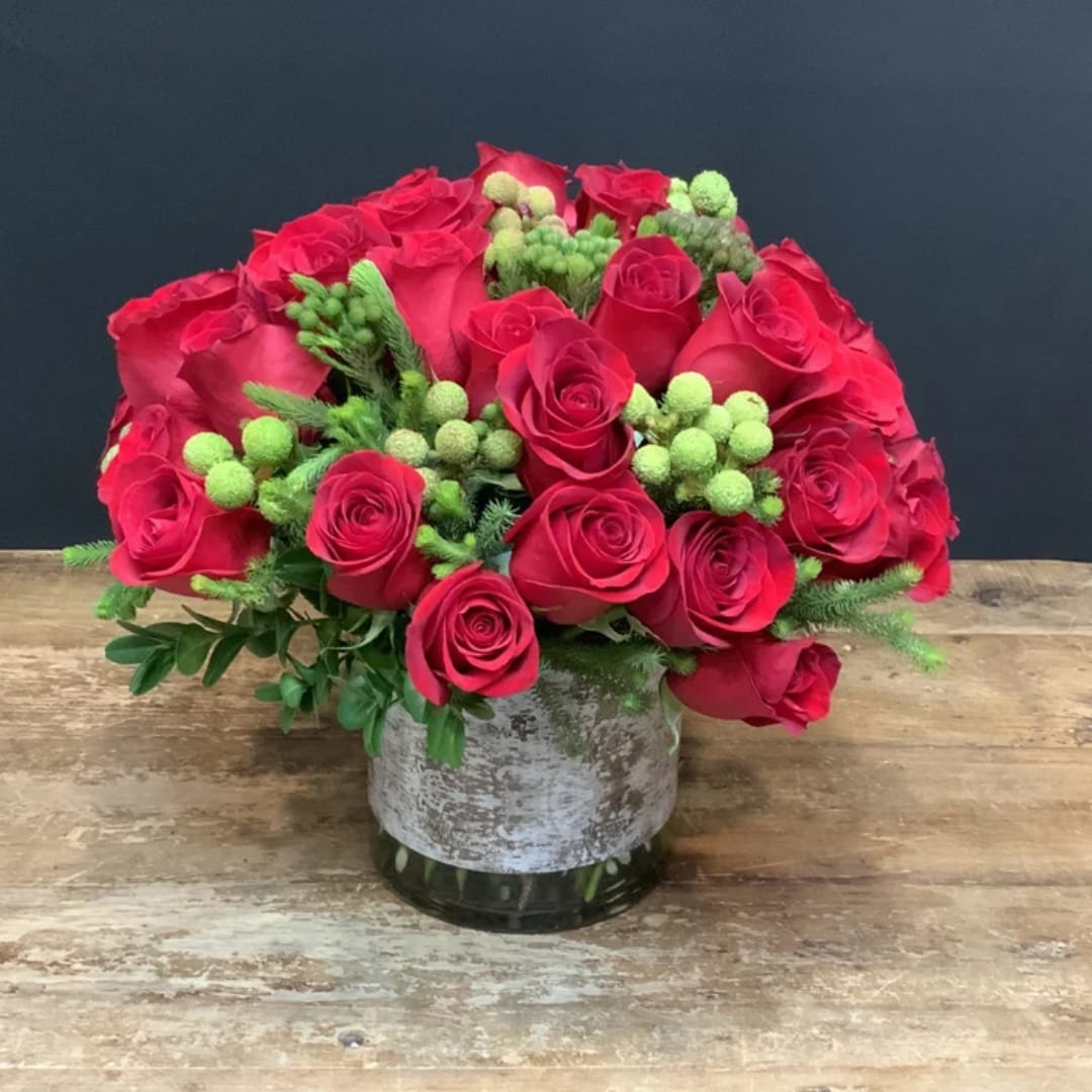Red rose bouquet in a glass vase with green berry accents