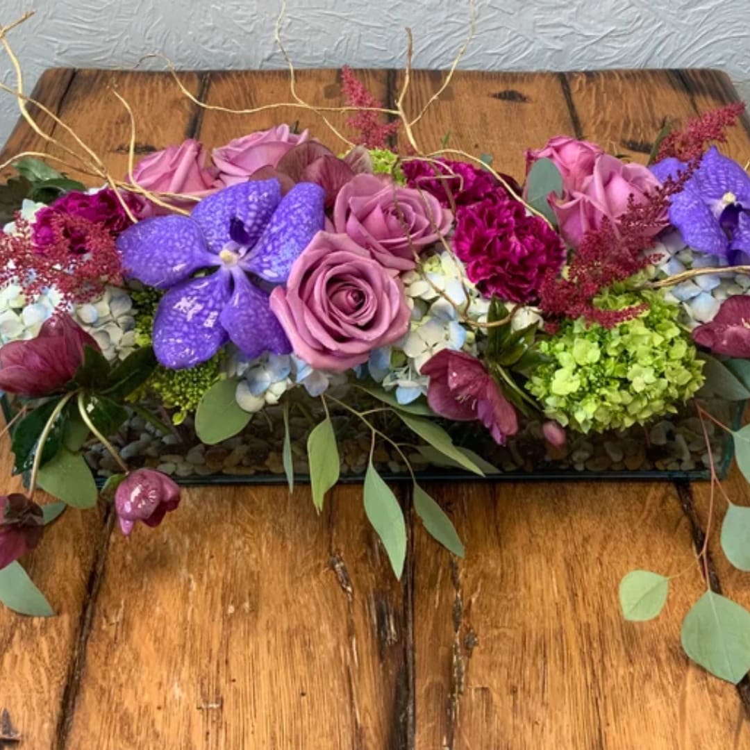 Purple and pink floral arrangement with roses and orchids on a wooden table