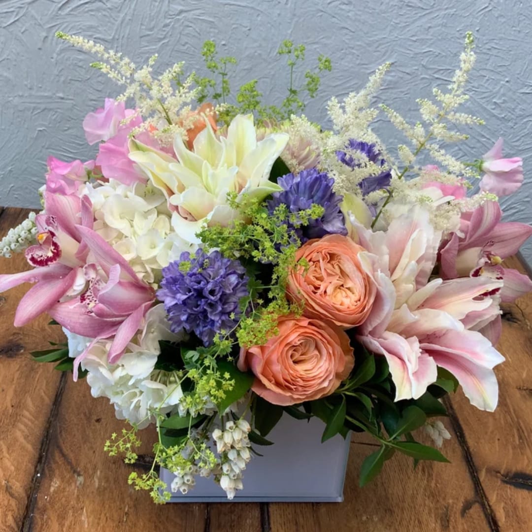 Mixed pastel bouquet with lilies, roses, and purple blooms in a white box