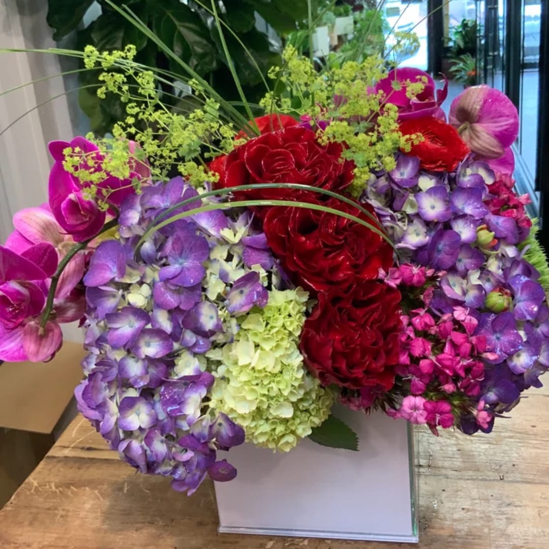 Colorful bouquet with red roses, purple hydrangeas, and pink orchids in a white box