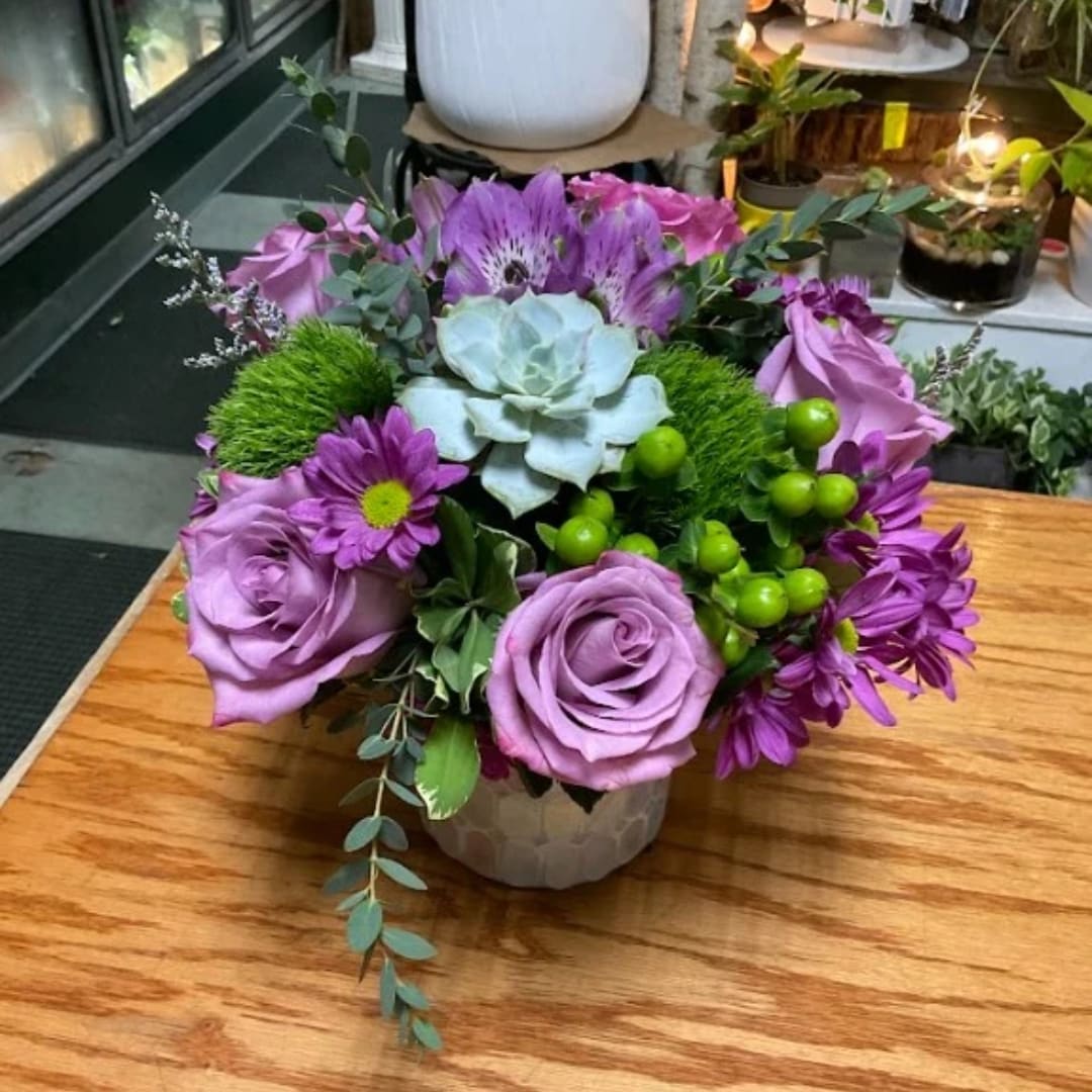 Purple roses and daisies arranged in a small vase with a succulent center