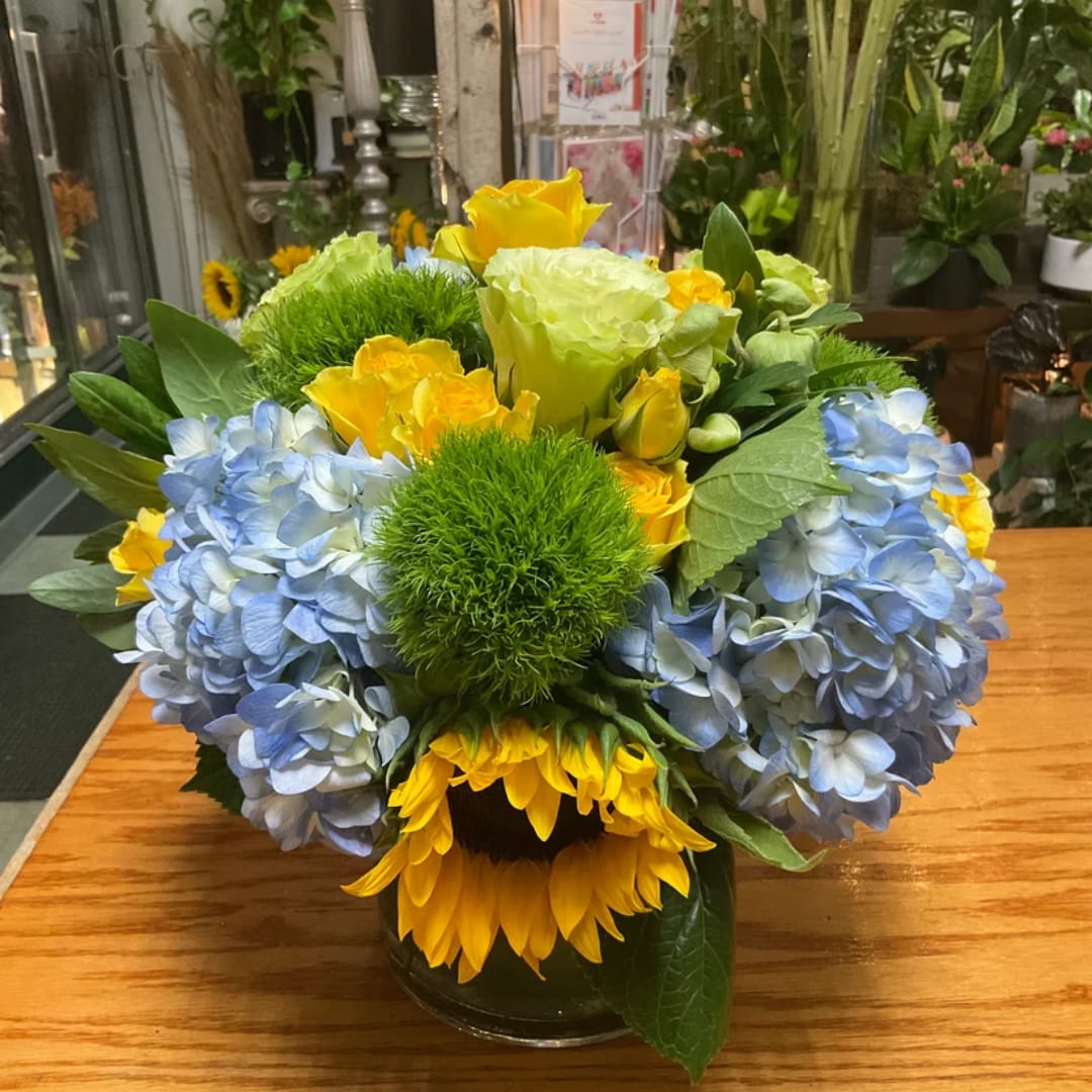 Blue hydrangeas and yellow roses in a glass vase with sunflowers