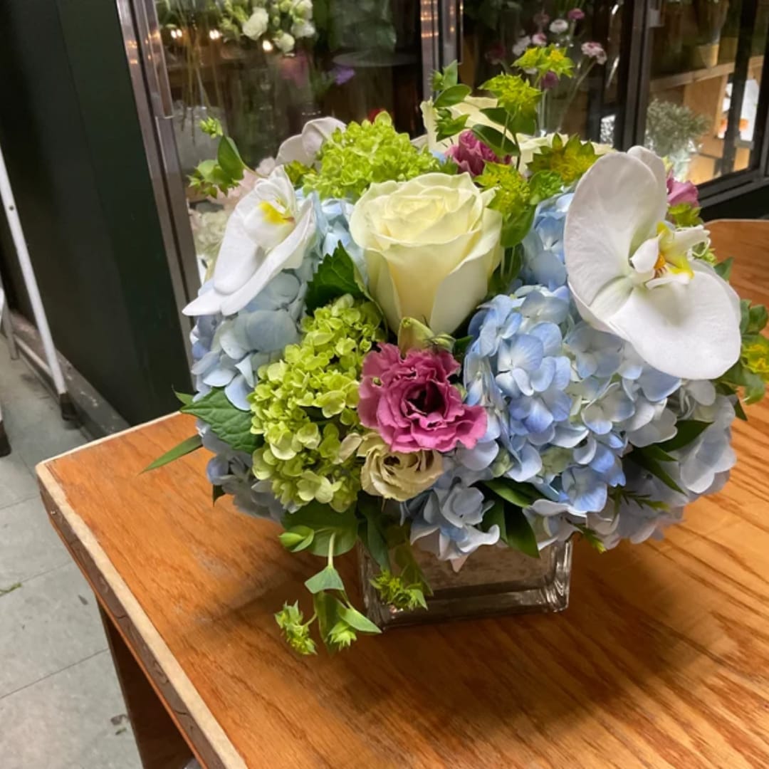 Blue hydrangea and white orchid bouquet in a square glass vase