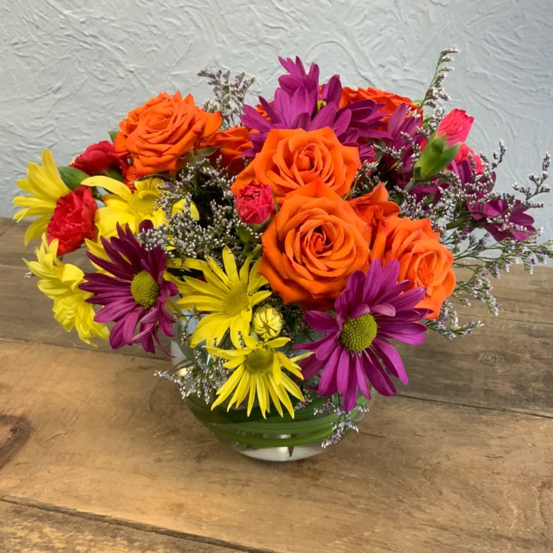 Colorful bouquet of orange roses, purple daisies, and yellow flowers in a glass vase