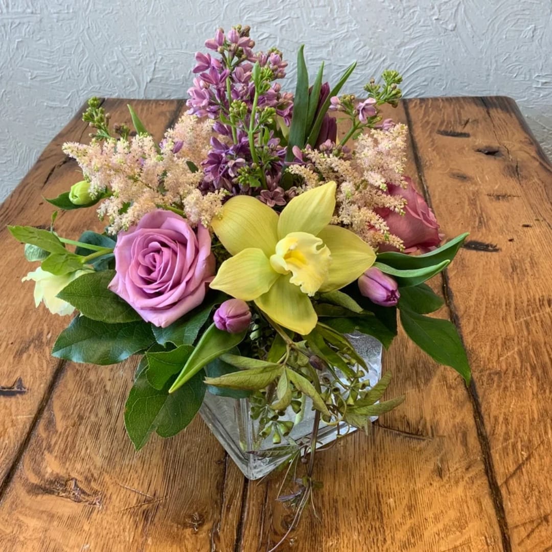 Lavender roses and yellow orchid arrangement in a clear glass vase