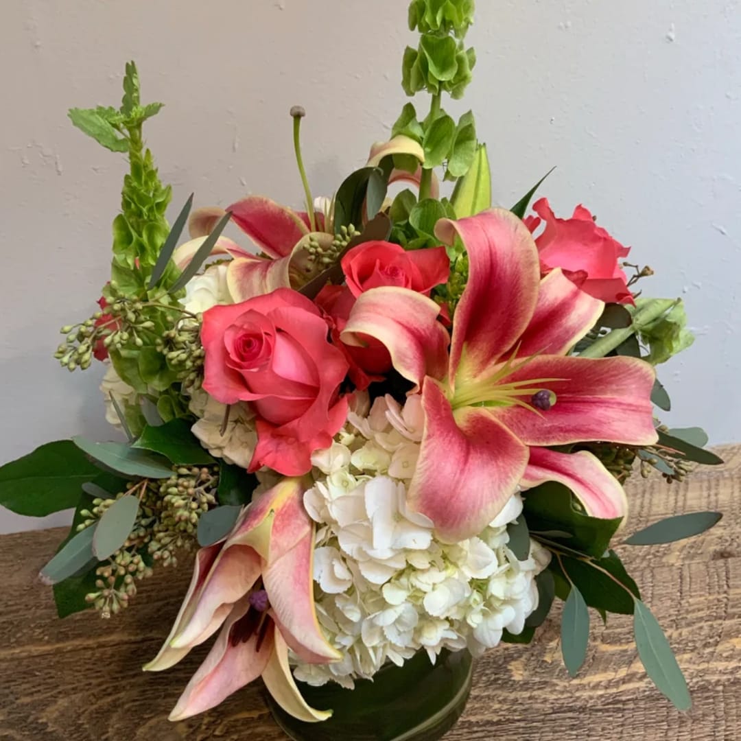 Pink roses and lilies arranged with white hydrangea in a glass vase