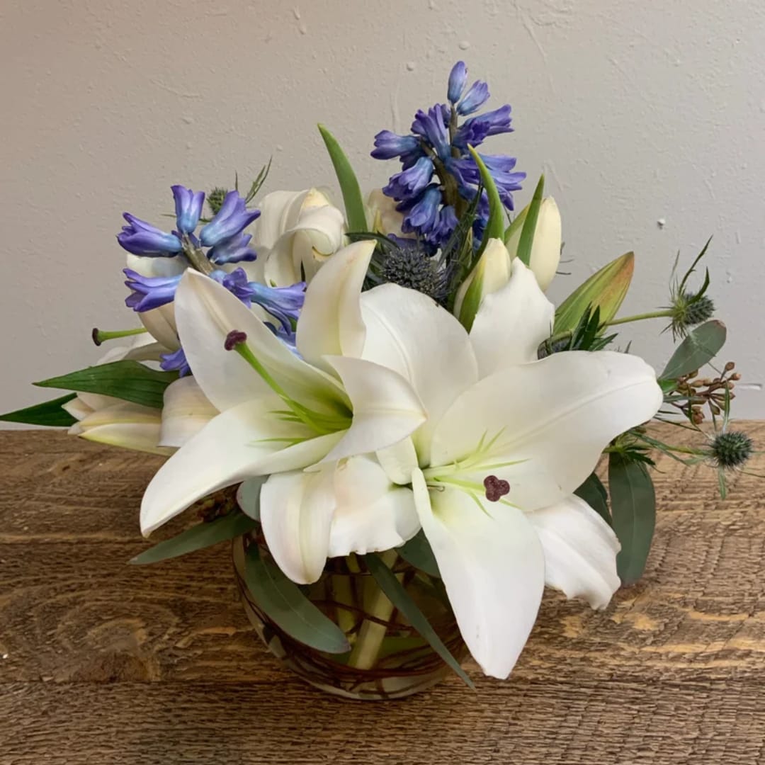 White lilies and blue flowers arranged in a glass vase