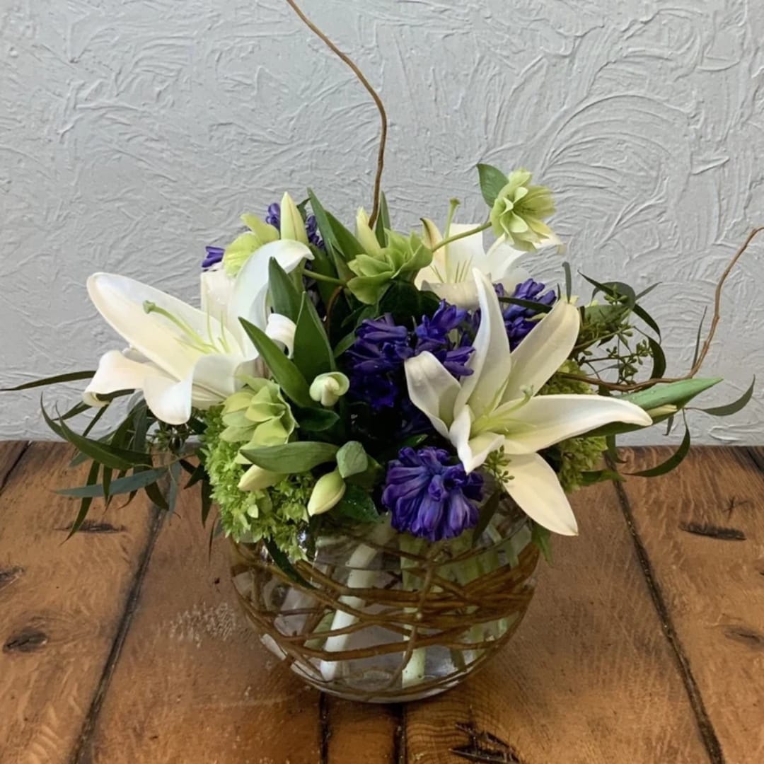 White lilies and purple flowers arranged in a glass bowl vase