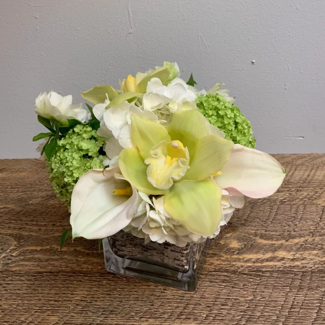 White and pale green floral arrangement in a square glass vase