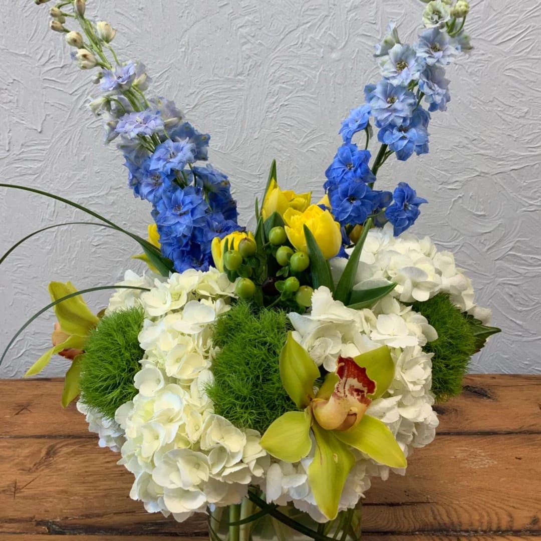 Blue delphinium and white hydrangea arrangement with yellow orchids in a vase