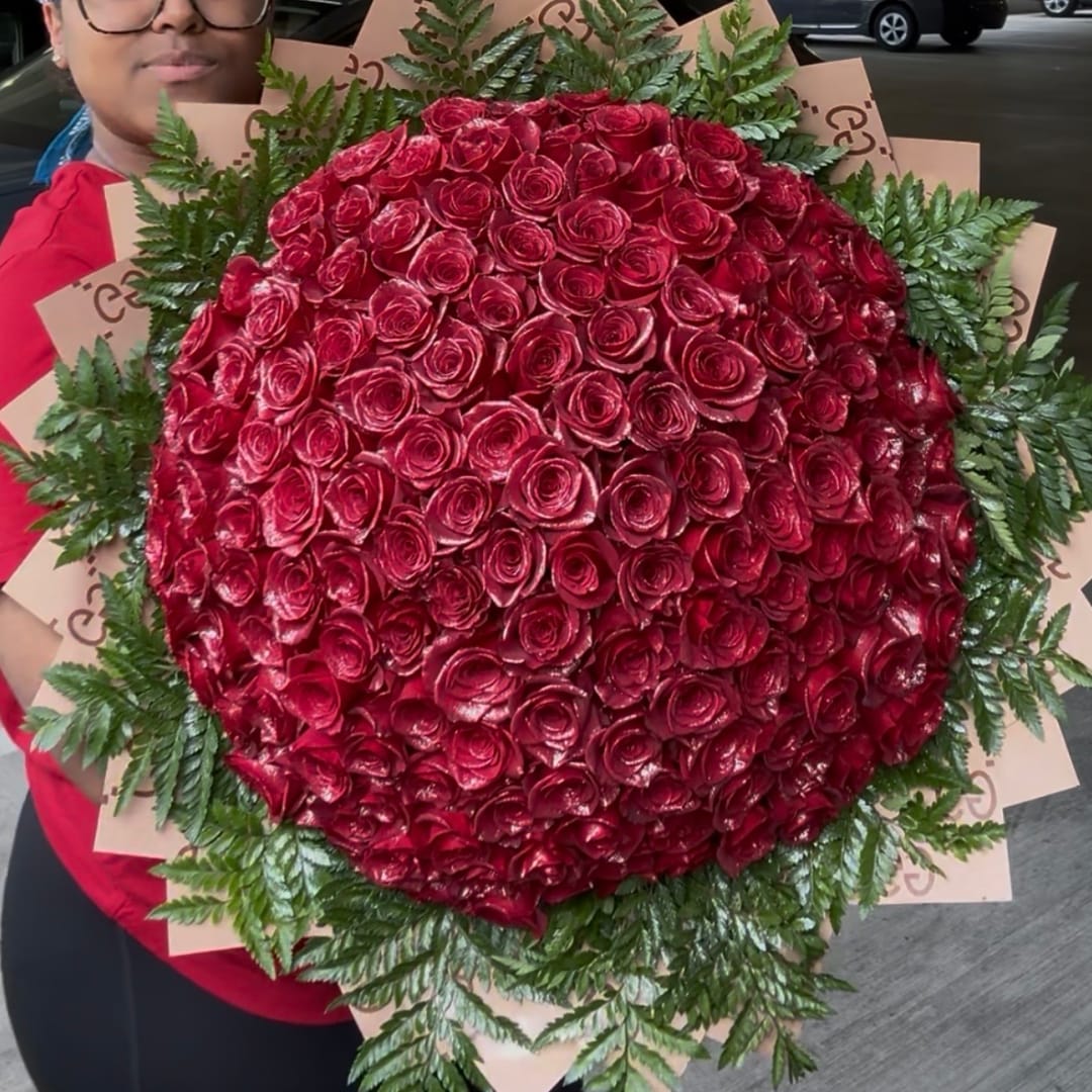 Large bouquet of red roses with fern foliage, held by a person