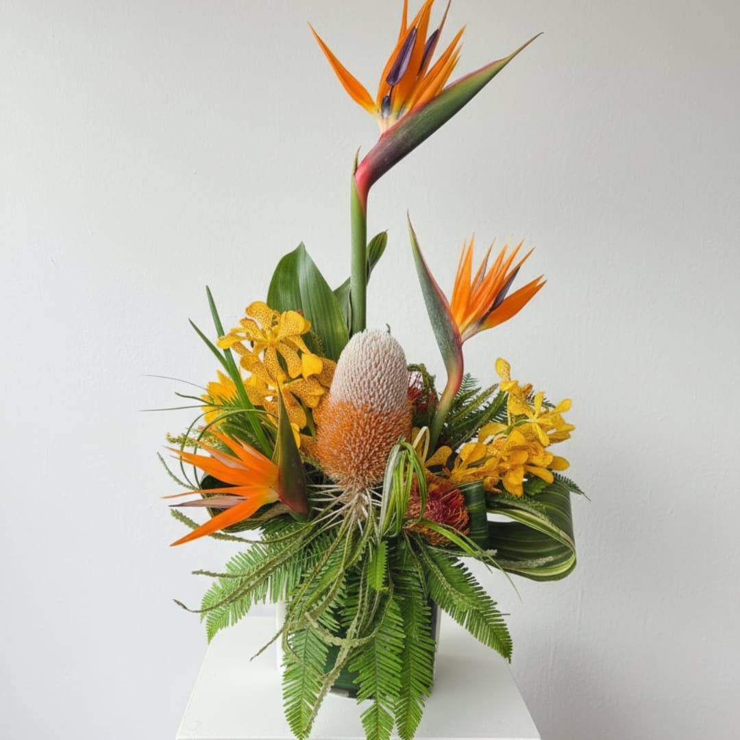 Tropical arrangement with orange bird of paradise and yellow blooms in a vase