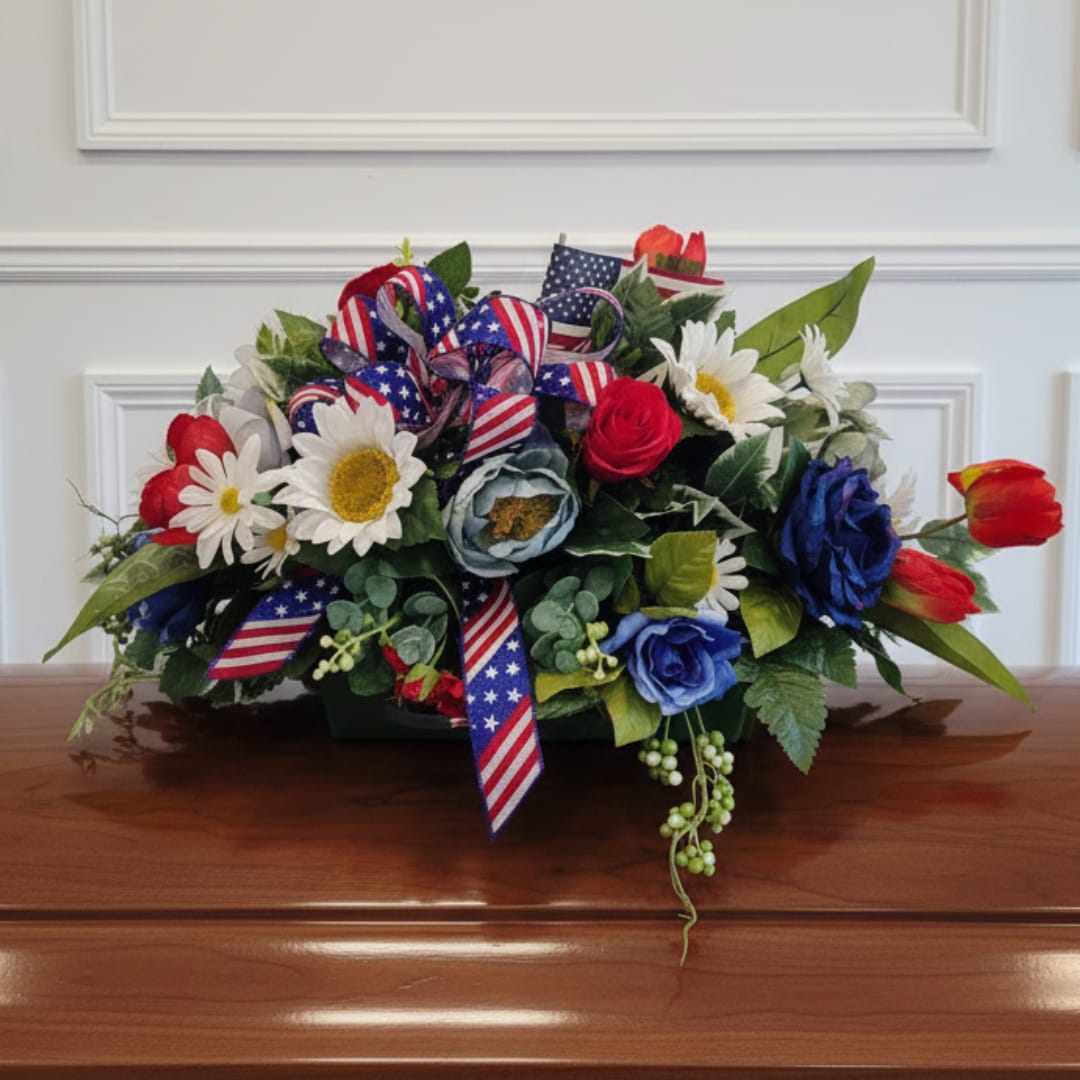 Patriotic floral arrangement with daisies, roses, and ribbon in a low container