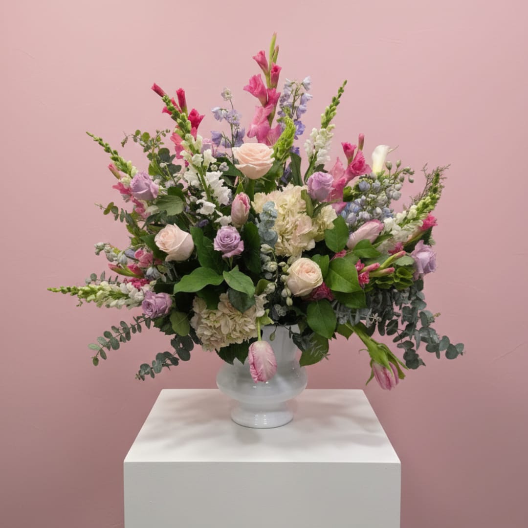 Mixed pastel bouquet in a frosted glass vase on a white pedestal