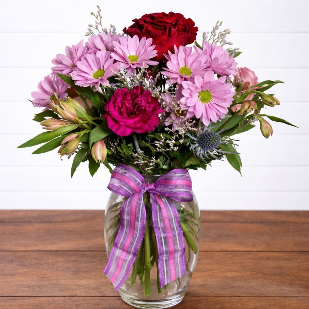 Mixed pink and red flowers in a clear glass vase with a purple ribbon