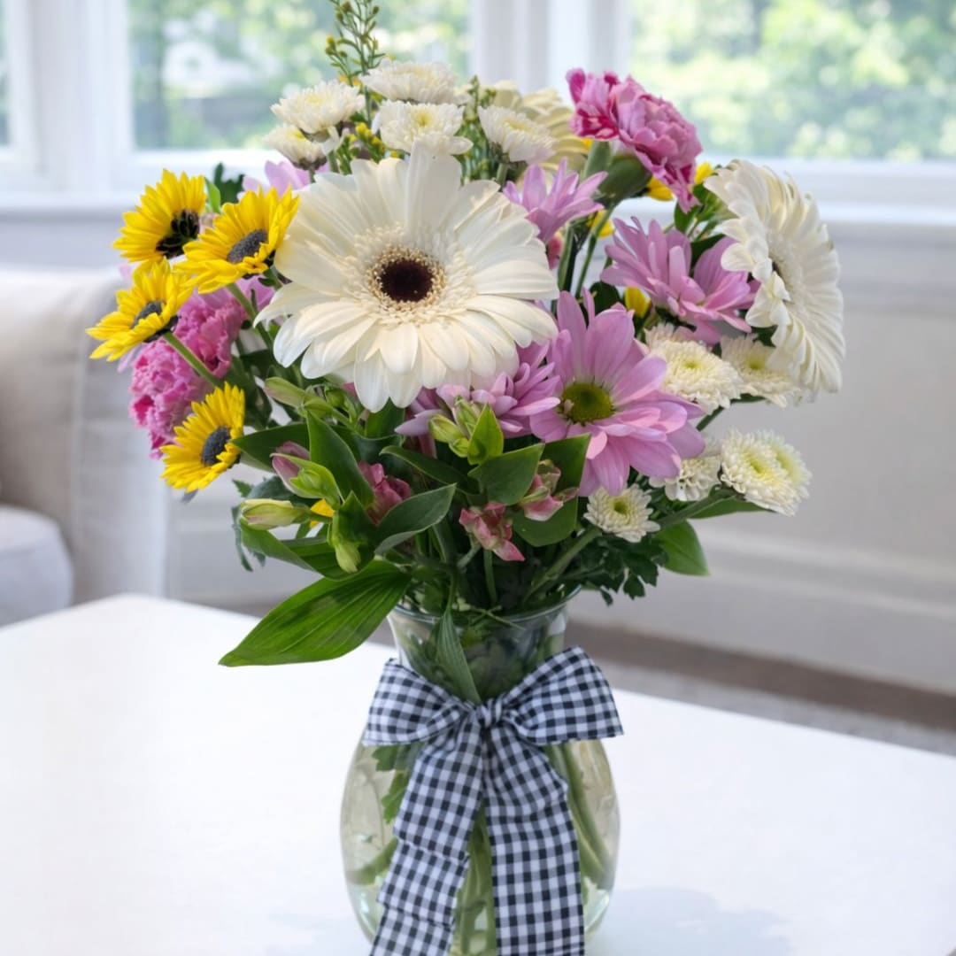 Mixed bouquet of daisies and sunflowers in a glass vase with a checkered ribbon