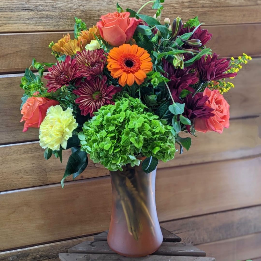 Mixed bouquet of orange, pink, purple, and green flowers in a glass vase