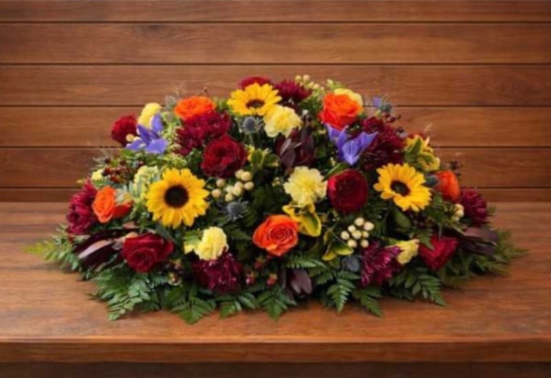 Low floral arrangement with sunflowers, roses, and mixed blooms on a wooden surface