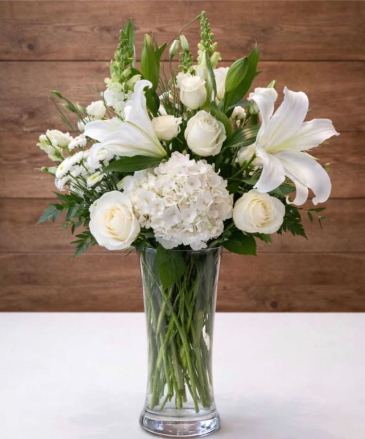 White floral arrangement in a clear glass vase with roses and lilies