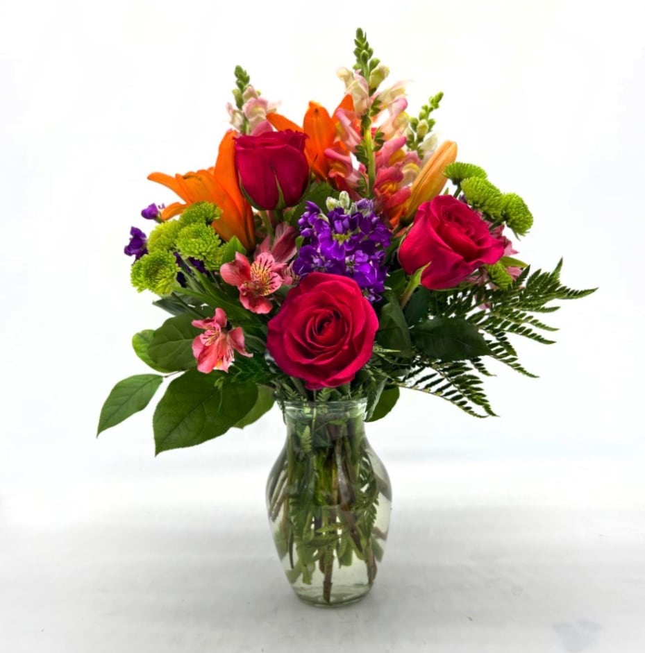 Mixed bouquet of roses, lilies, and purple flowers in a glass vase