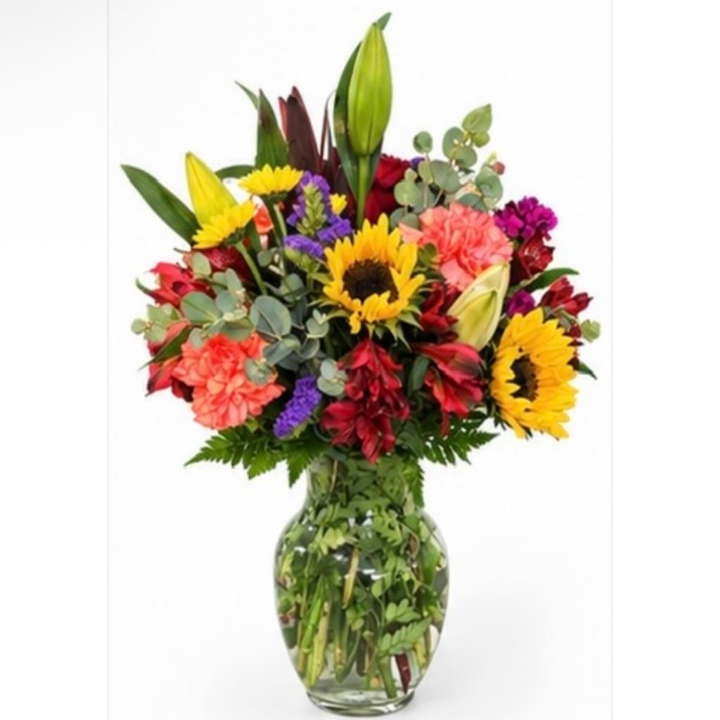 Mixed bouquet of sunflowers, lilies, and carnations in a glass vase