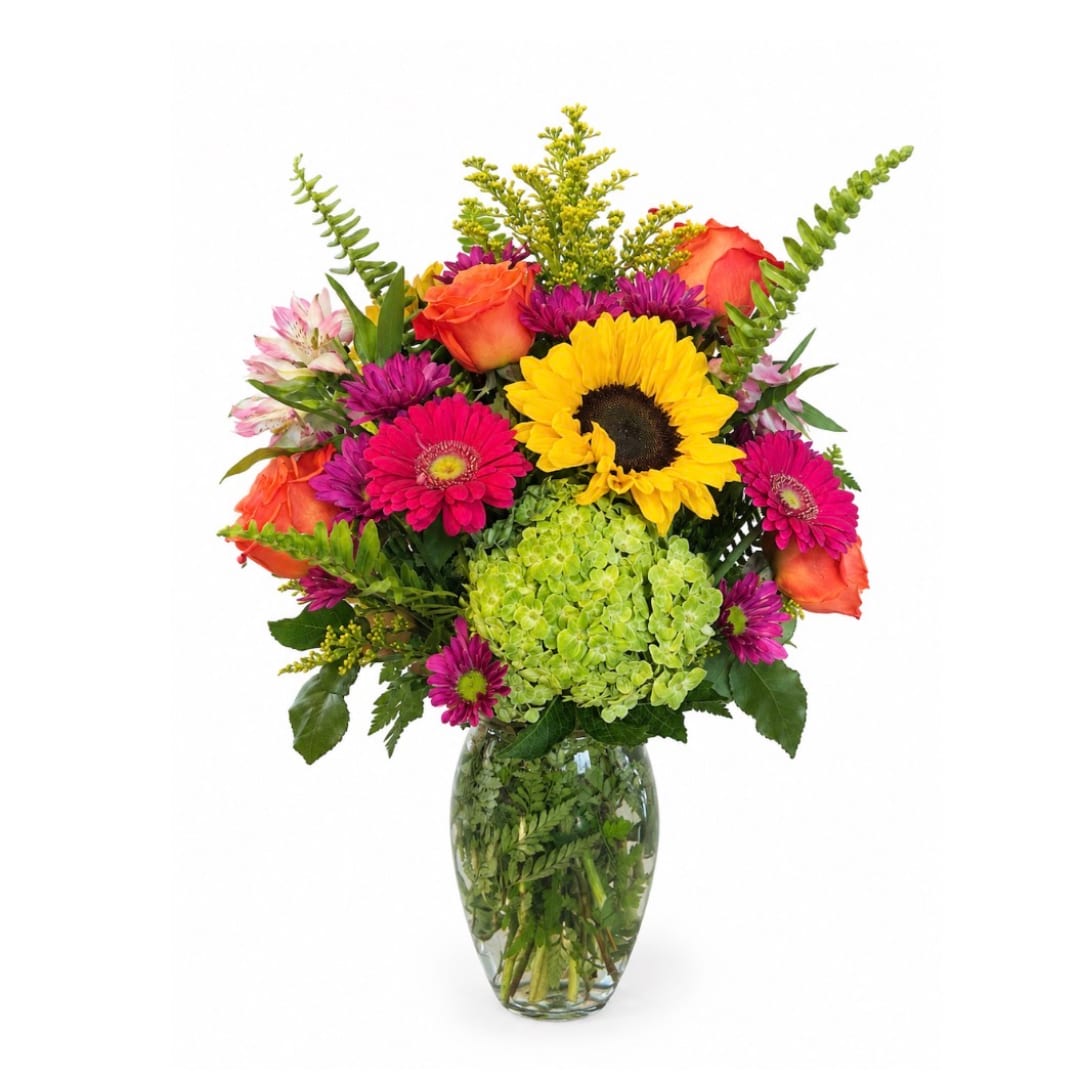 Mixed bouquet with sunflowers, roses, and pink daisies in a glass vase