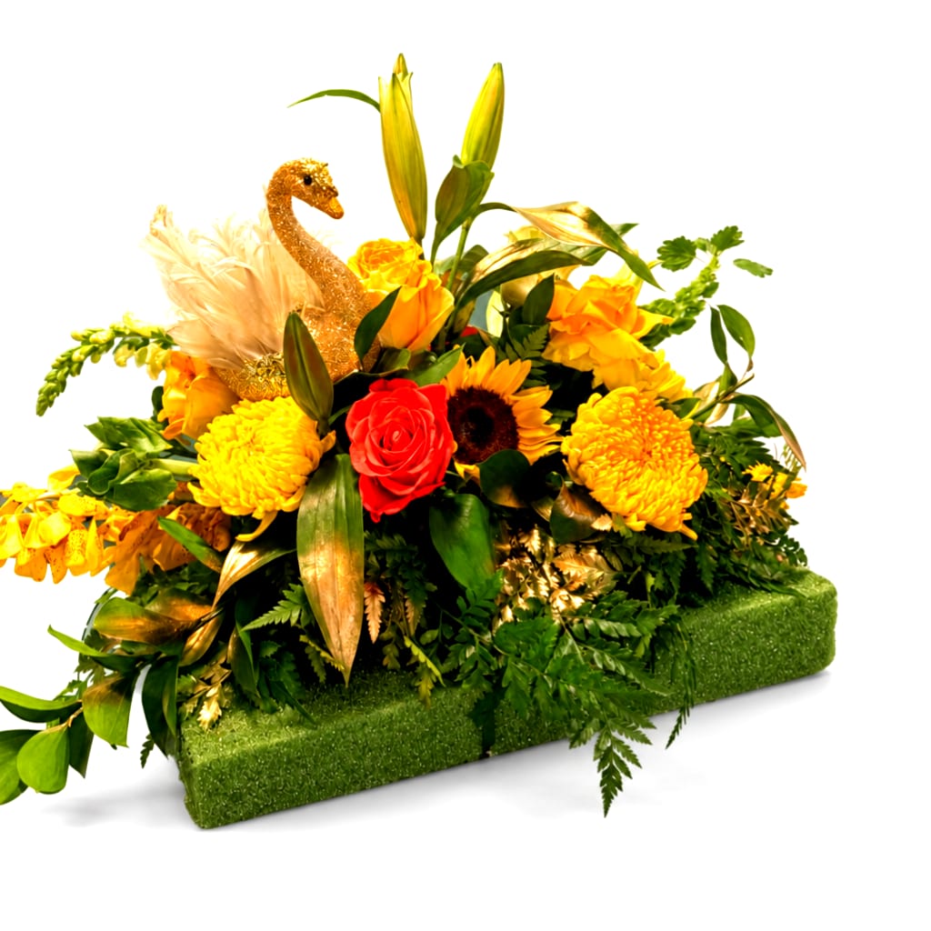Yellow and red floral arrangement with a gold swan accent on a green base