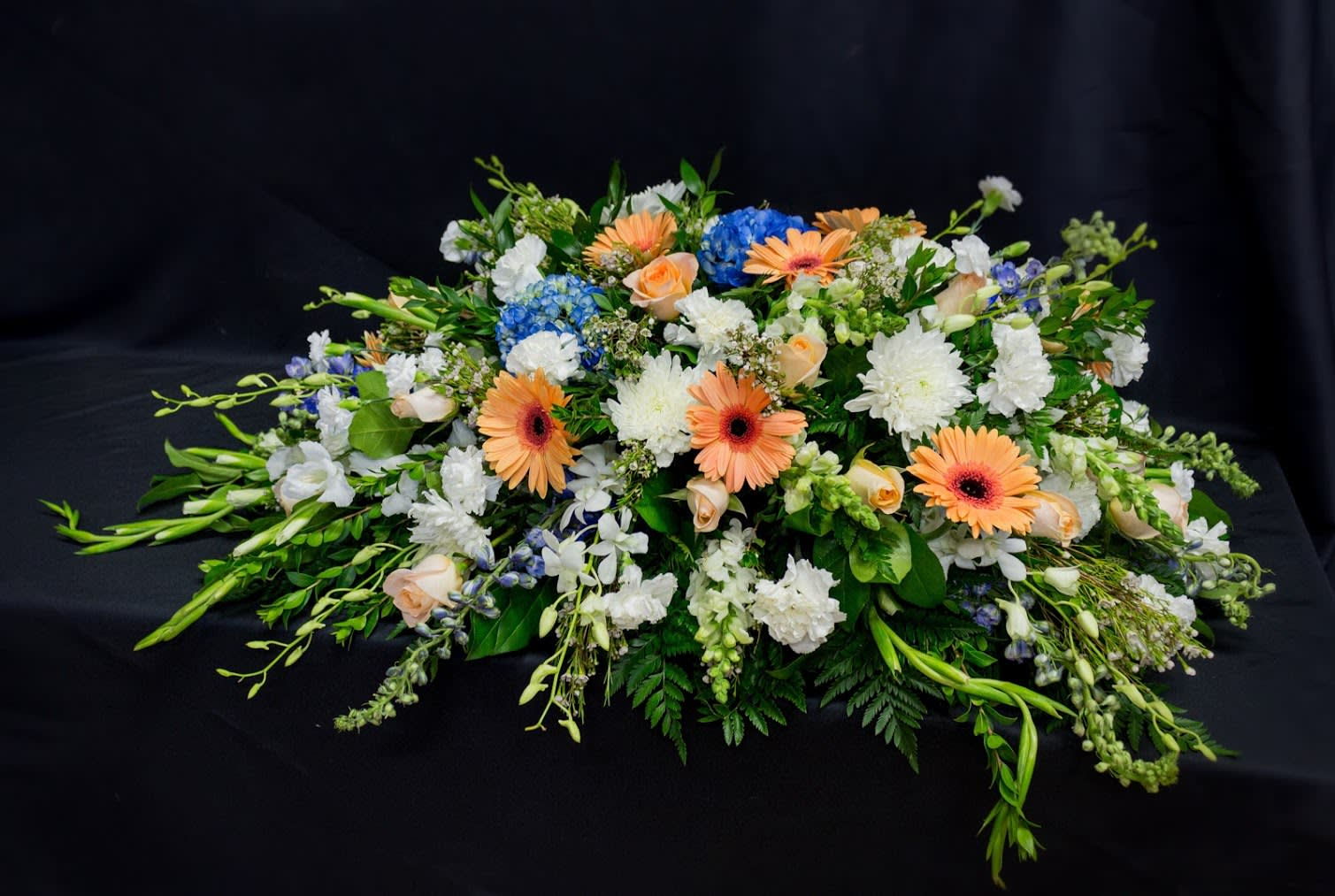 Low floral spray with peach gerberas, white blooms, and blue hydrangeas